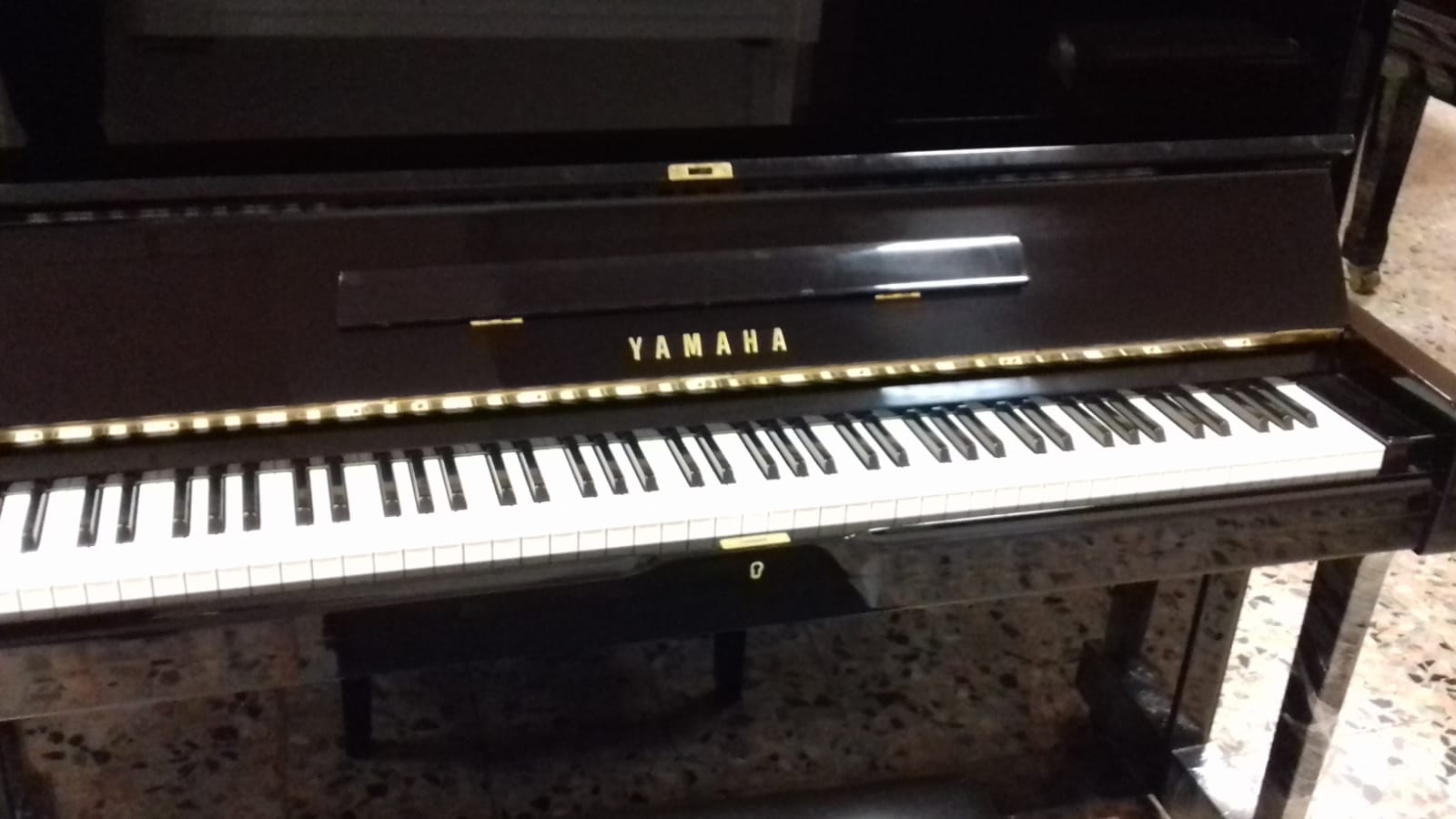 Un pianoforte Yamaha è appoggiato su un pavimento piastrellato