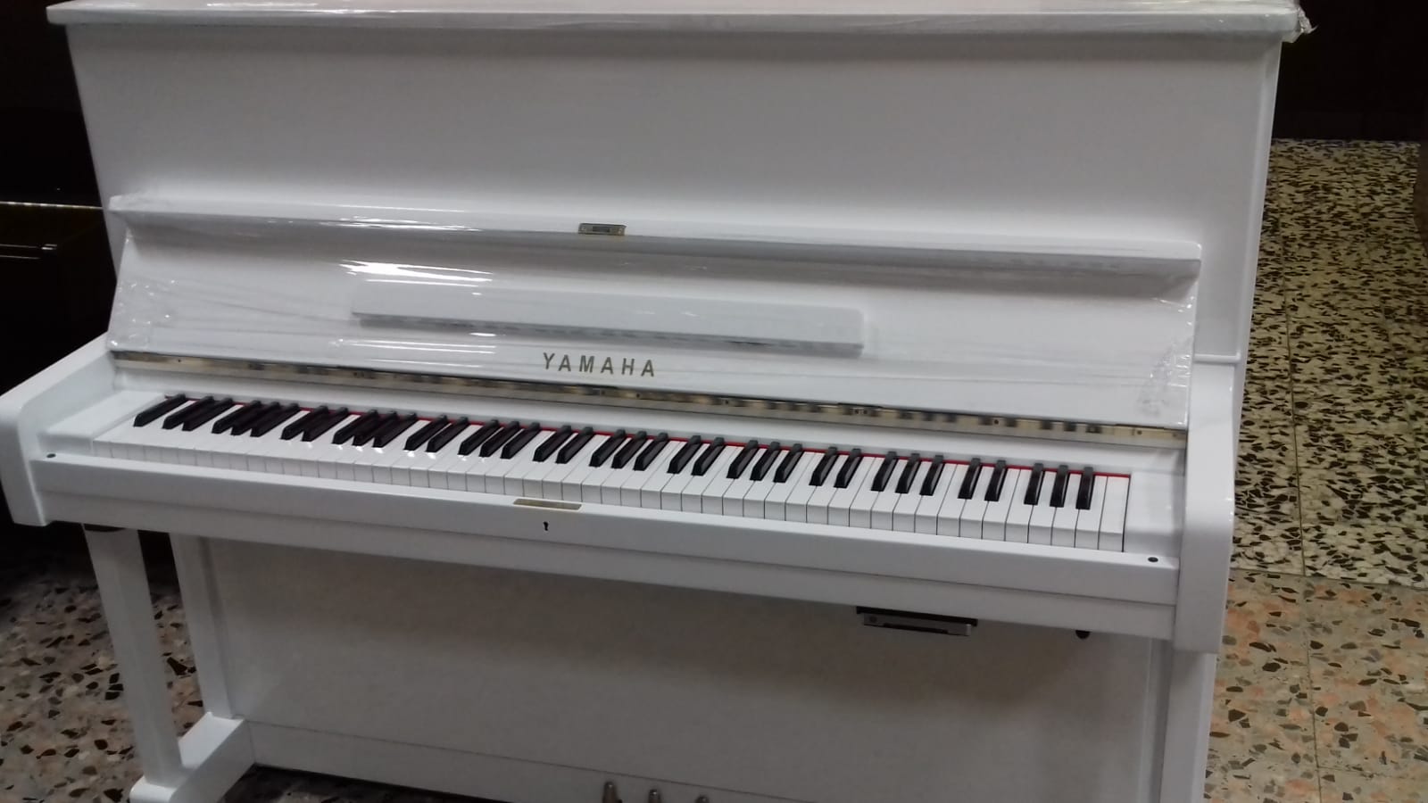 Un pianoforte verticale bianco è appoggiato su un pavimento piastrellato