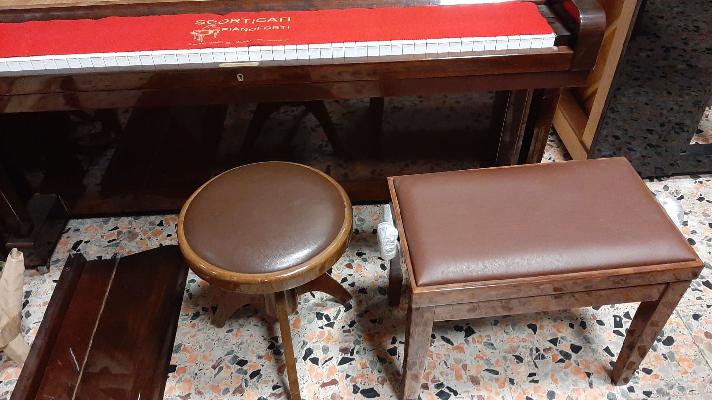 Uno sgabello marrone è appoggiato accanto a un pianoforte su un pavimento piastrellato