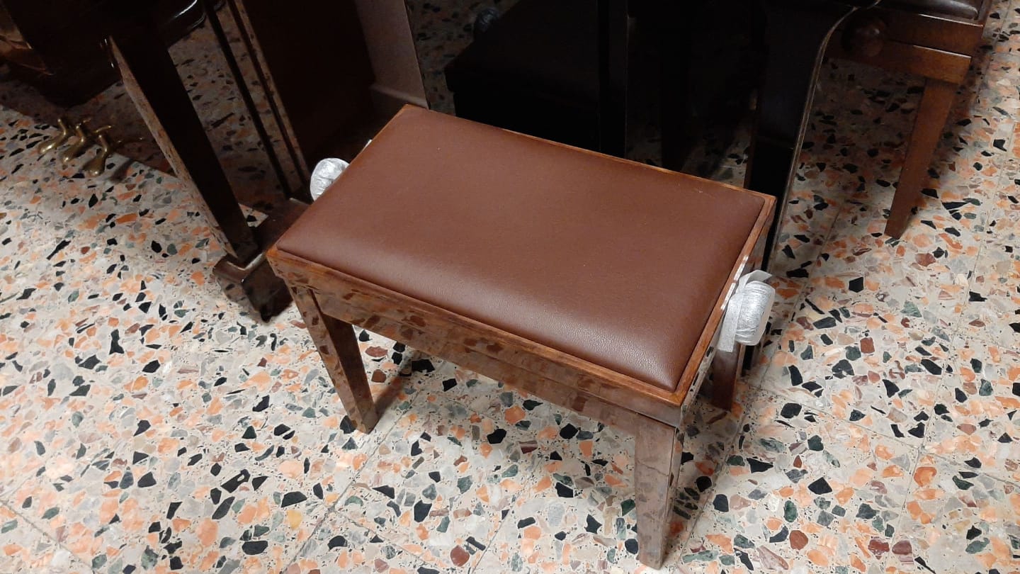 Uno sgabello marrone è appoggiato su un pavimento piastrellato accanto a un pianoforte