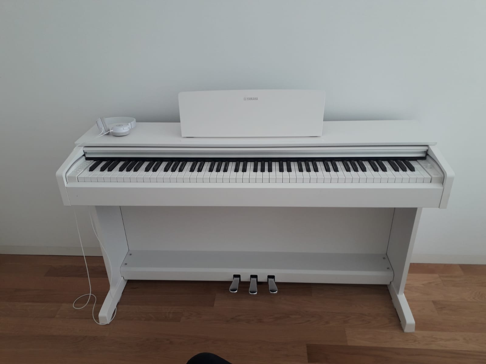 Un pianoforte bianco è appoggiato su un pavimento di legno in una stanza.