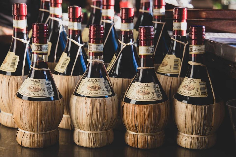 Bottiglie di liquido scuro con tappi rossi, in portacannucce, su un bancone.