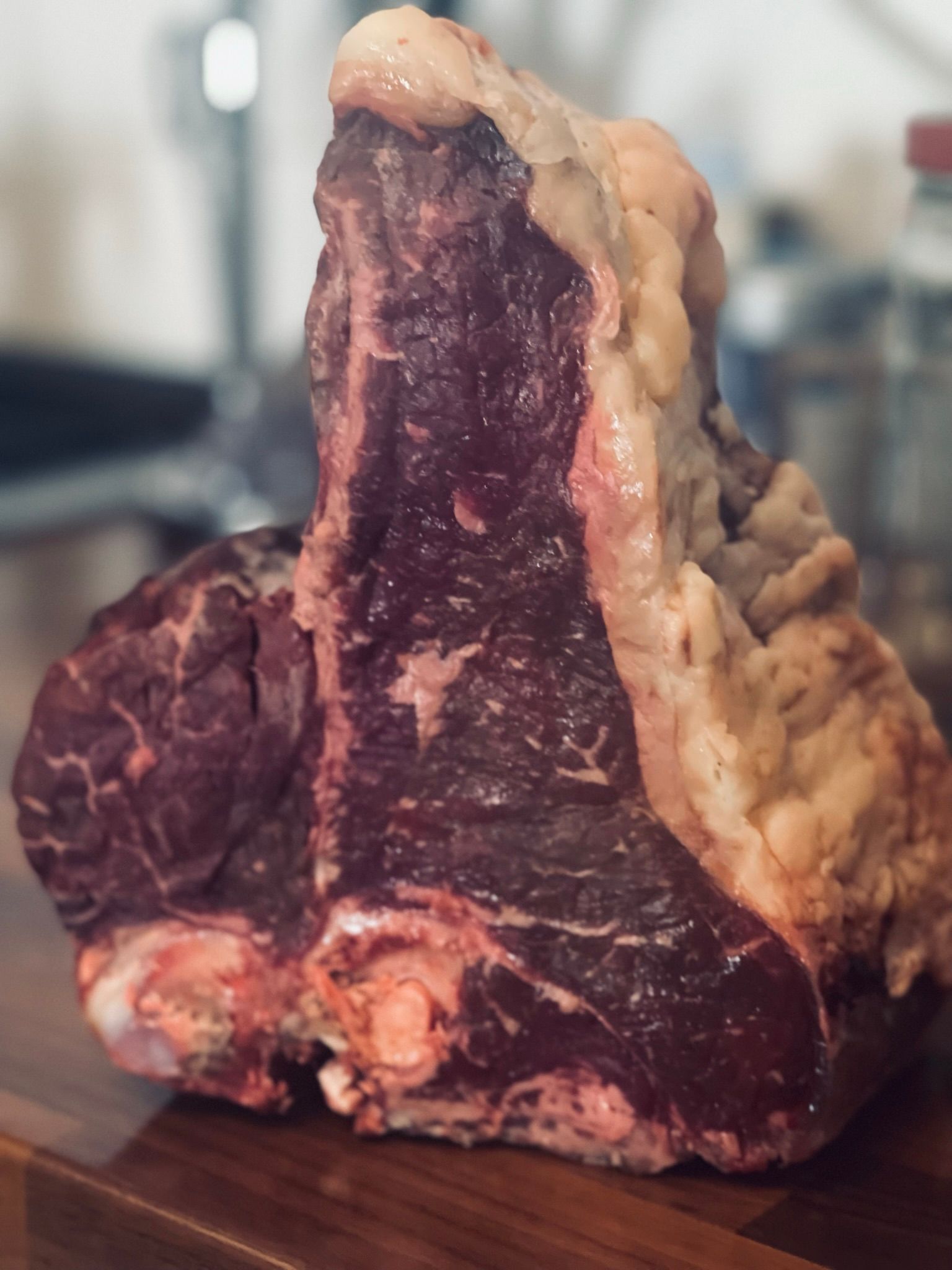 Grande bistecca cruda a T, taglio spesso con carne rosso scuro e grasso cremoso, su una superficie di legno.