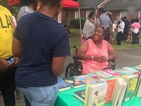 A woman in a wheelchair is sitting at a table with books on it at a LCRC event.