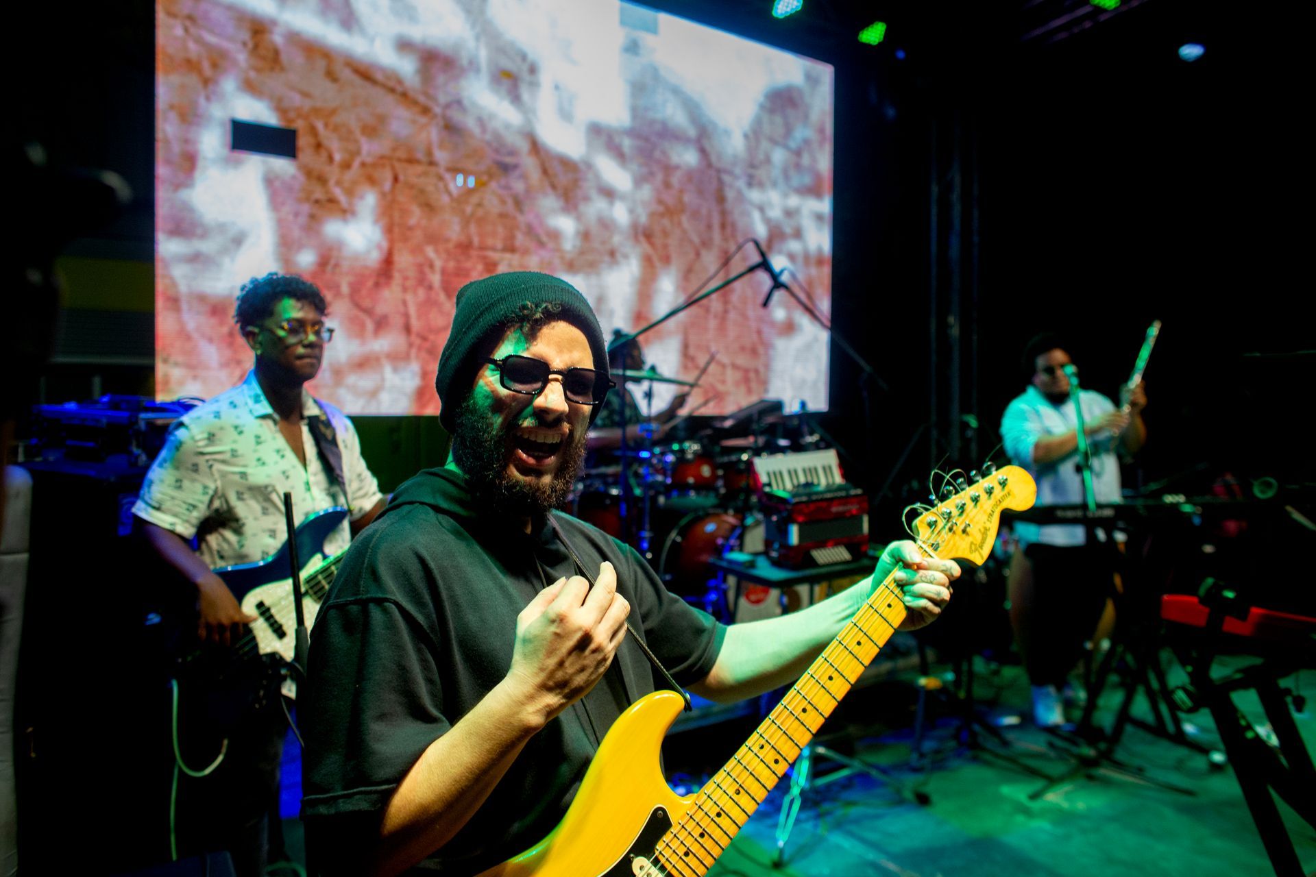 Un hombre está tocando una guitarra en un escenario frente a una pantalla grande.