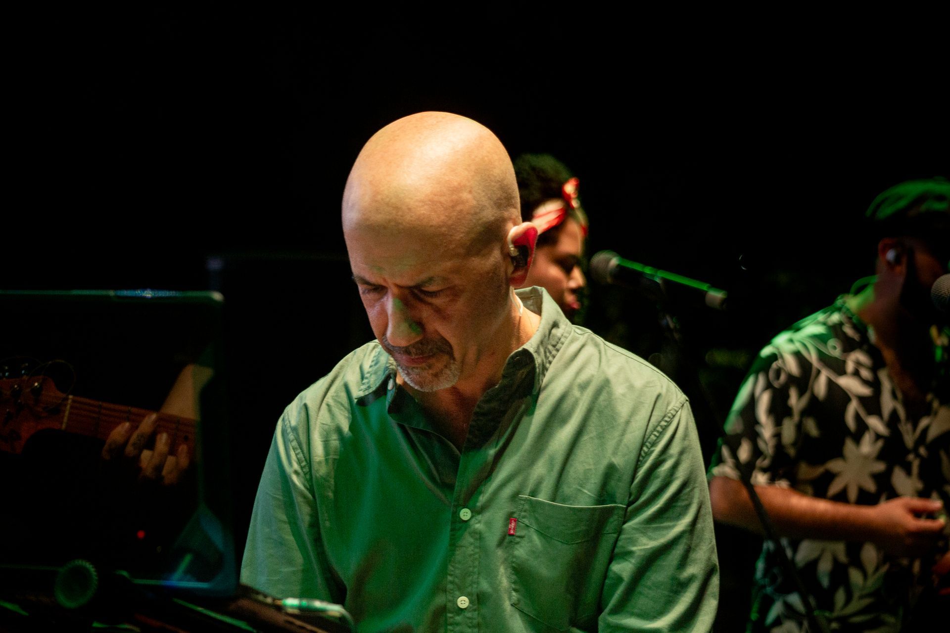 Un hombre calvo con una camisa verde está tocando un teclado en un escenario.