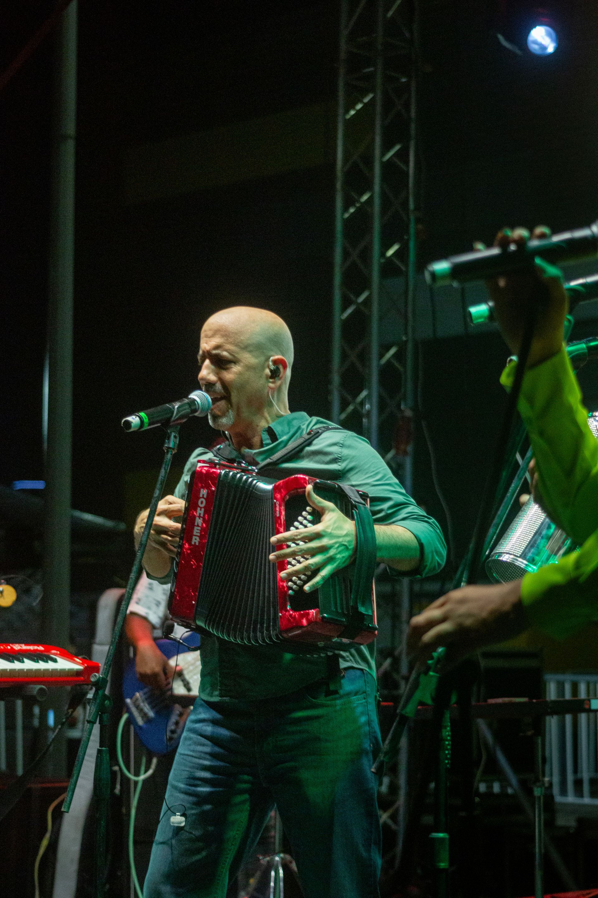 Un hombre toca el acordeón y canta en un micrófono en un escenario.