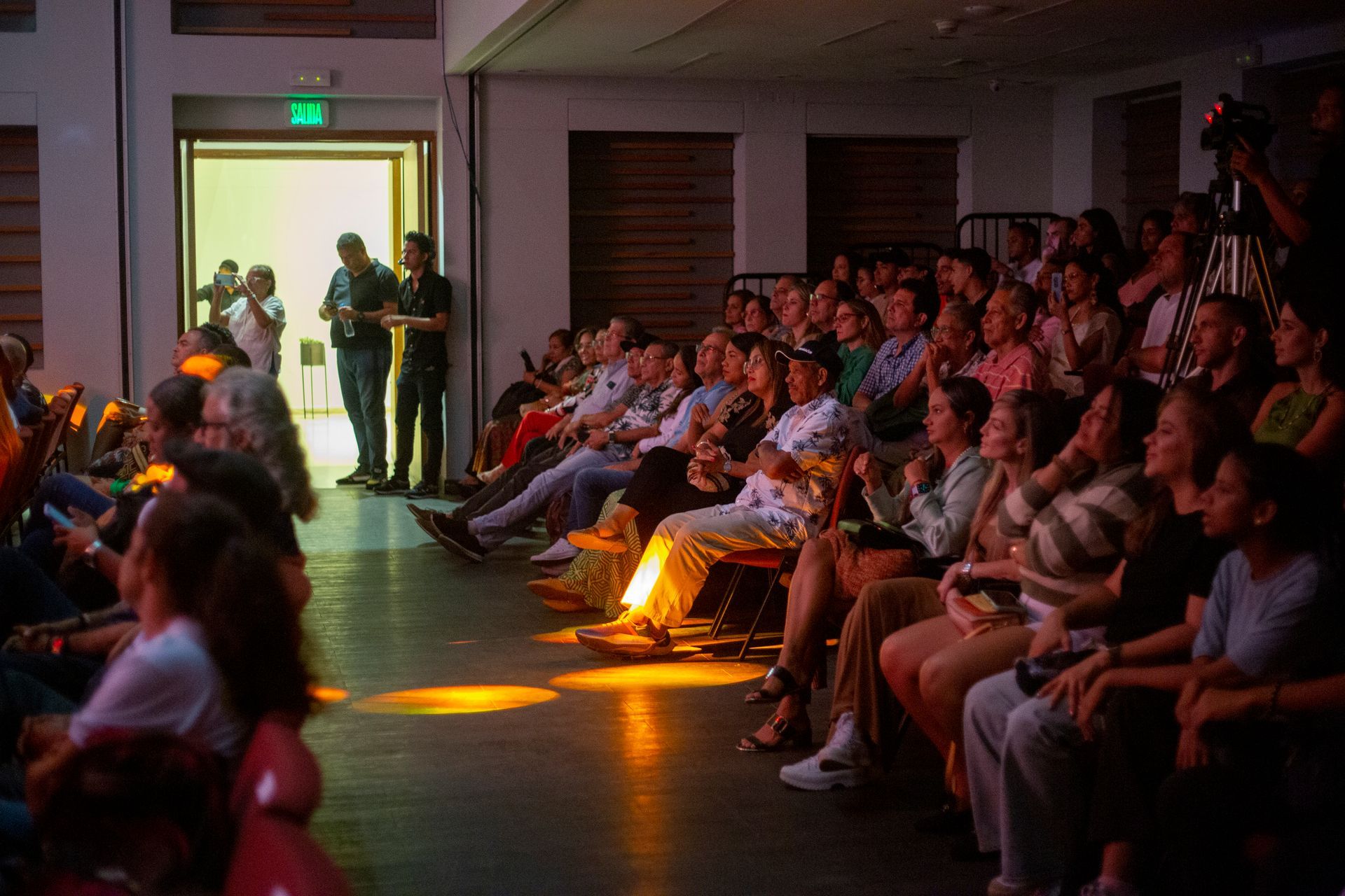Un grupo grande de personas está sentado en una habitación oscura viendo una película.