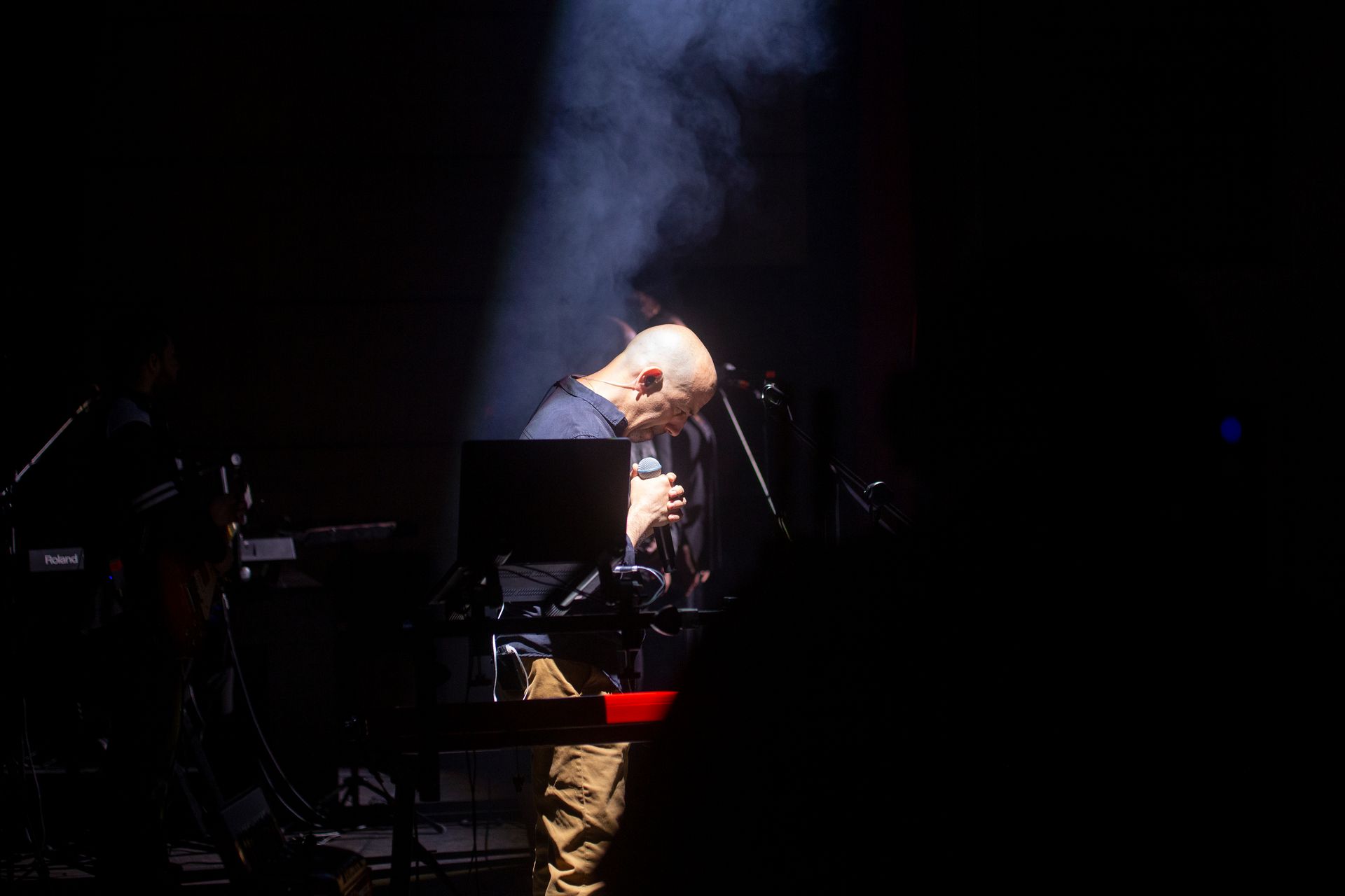 Un hombre está cantando en un micrófono en un escenario en la oscuridad.