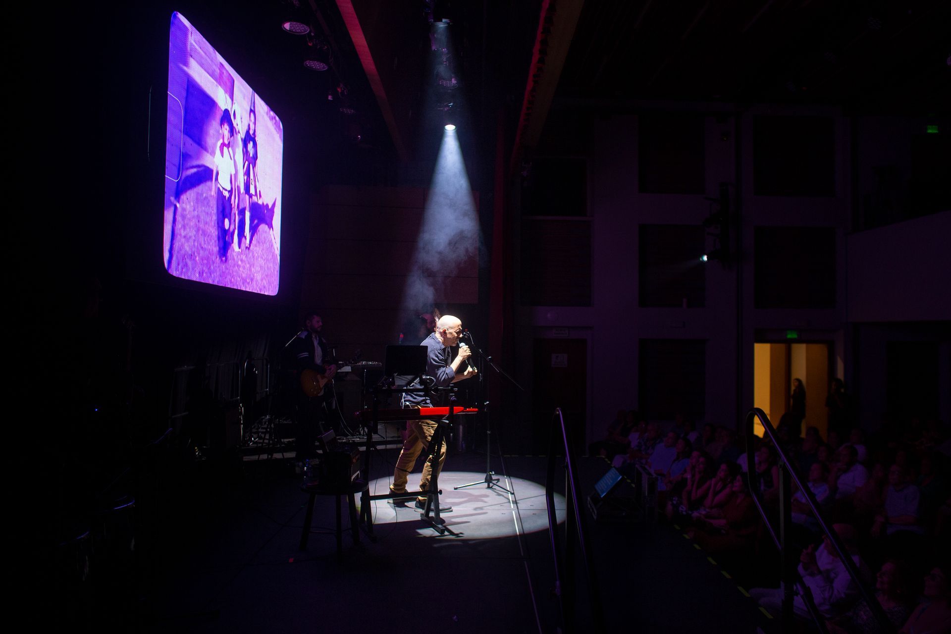 Un hombre está tocando un teclado en un escenario frente a una pantalla grande.