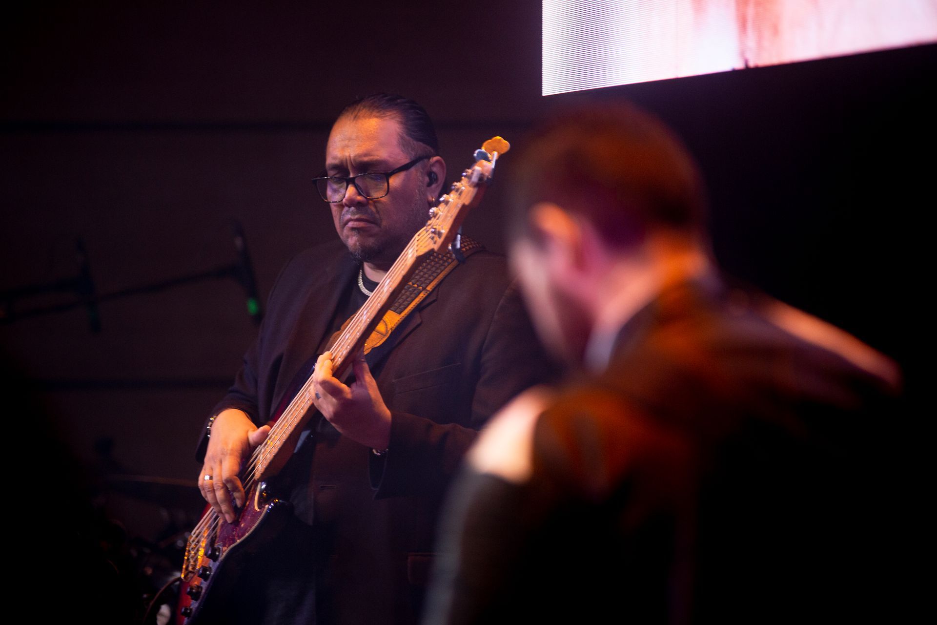 Un hombre de traje toca una guitarra en el escenario mientras otro hombre observa.