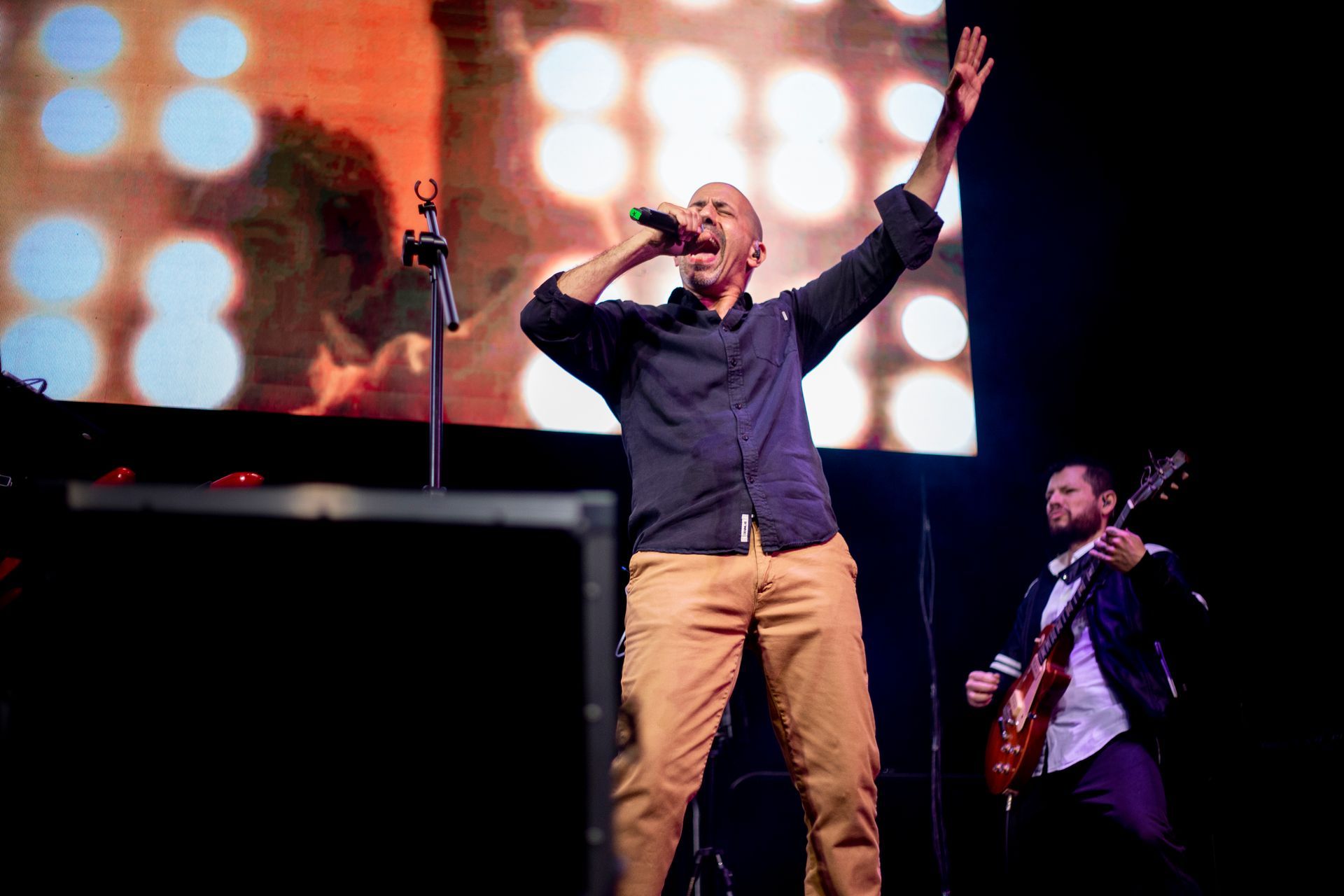 Un hombre está cantando en un micrófono en un escenario mientras otro hombre toca una guitarra.