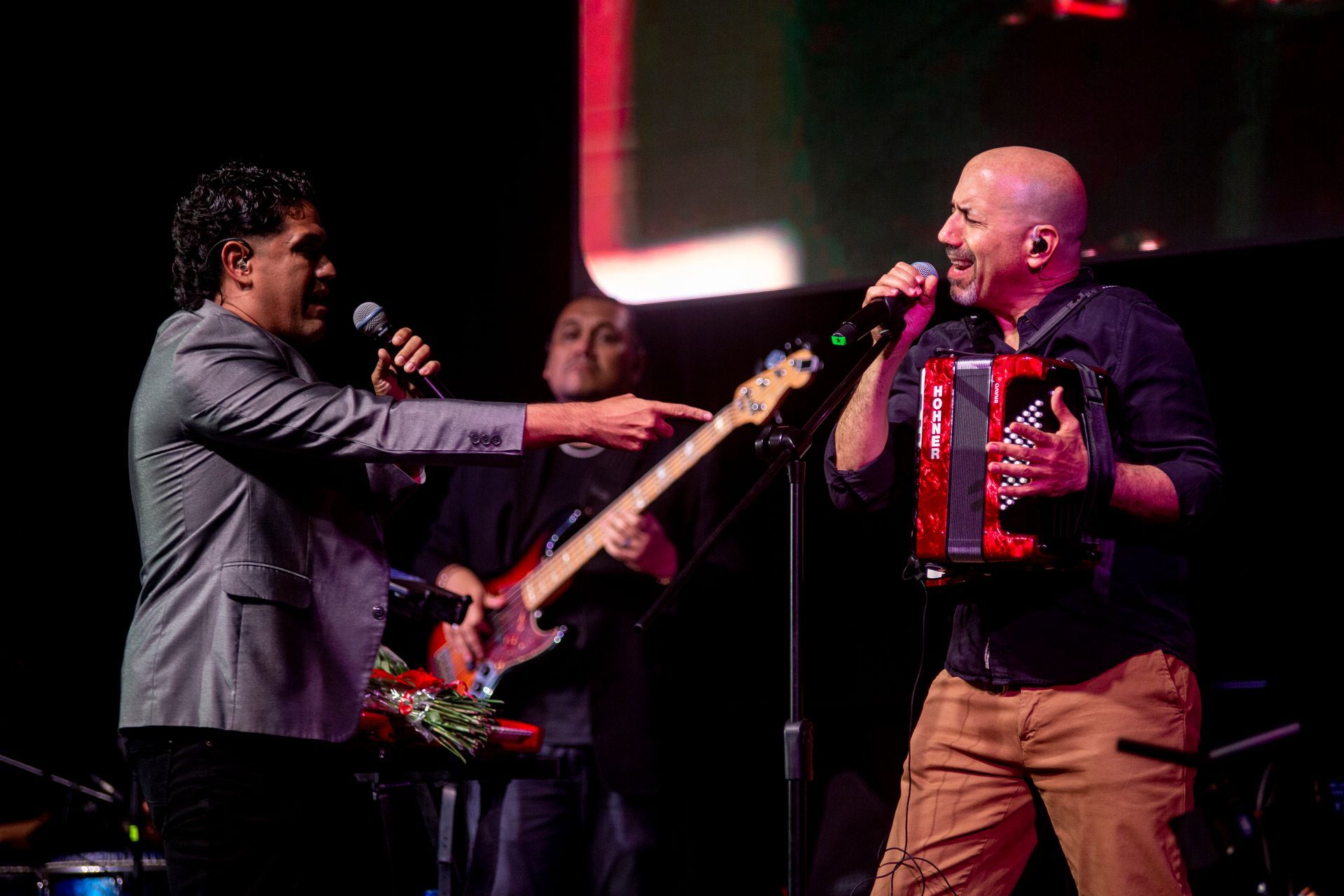 Un hombre canta en un micrófono mientras otro hombre toca el acordeón en el escenario.
