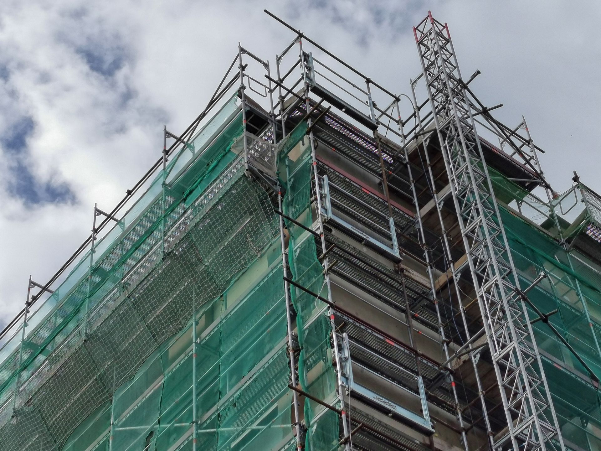 Cantiere con impalcature e reti verdi contro un cielo nuvoloso.