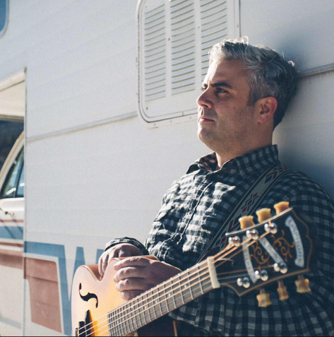 A man leaning against a wall holding a guitar