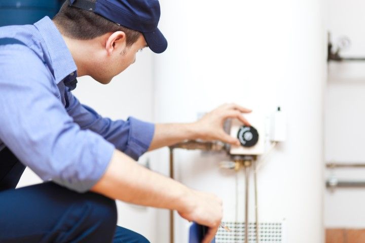 Plumber in blue uniform inspecting a wall-mounted water heater and pipes with a wrench