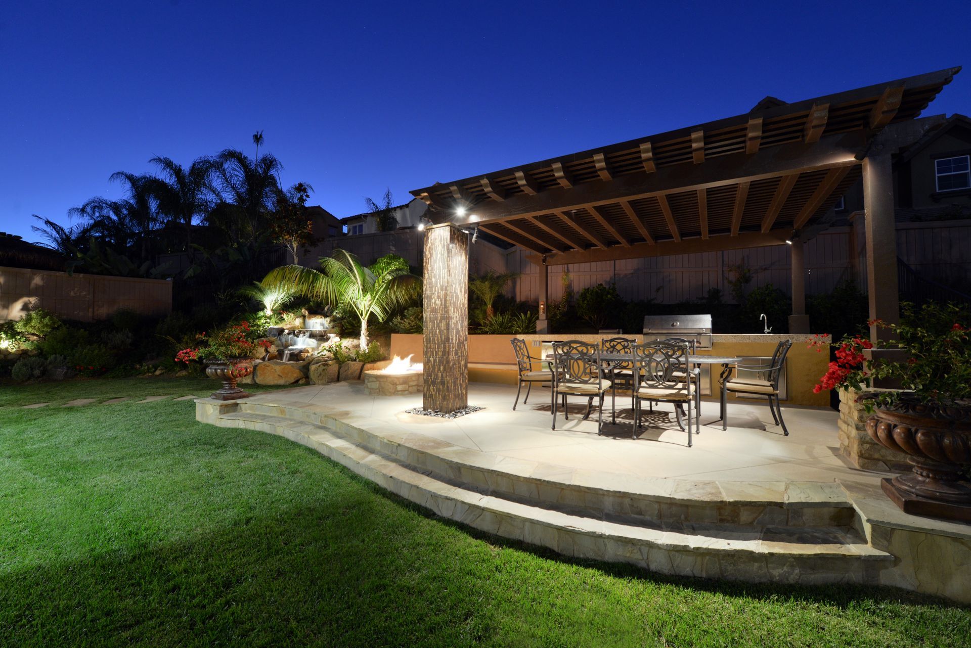 A patio with a table and chairs under a pergola at night