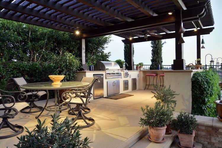 A patio with a table and chairs and a grill under a pergola.