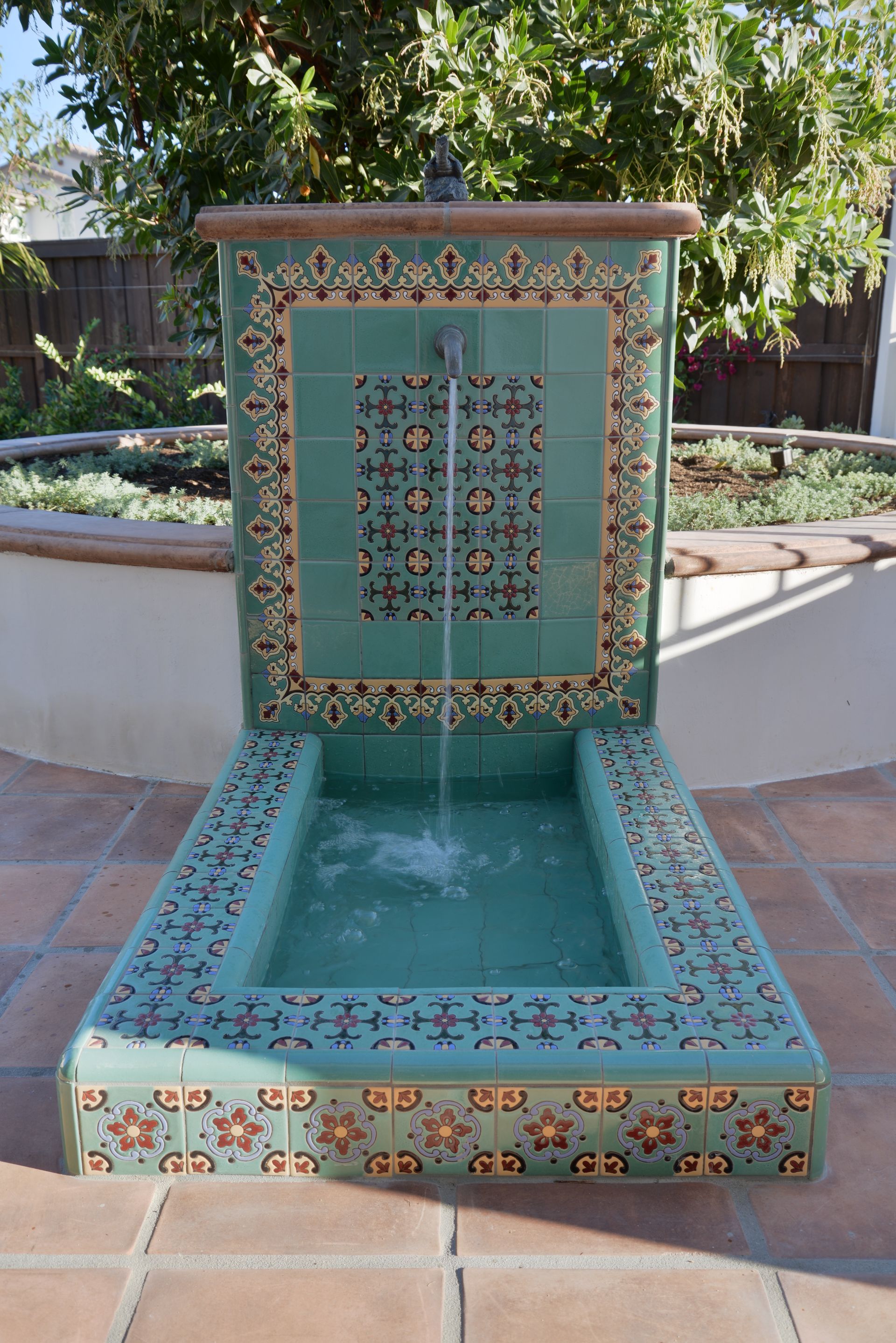A water fountain is sitting on a tiled floor in a garden.