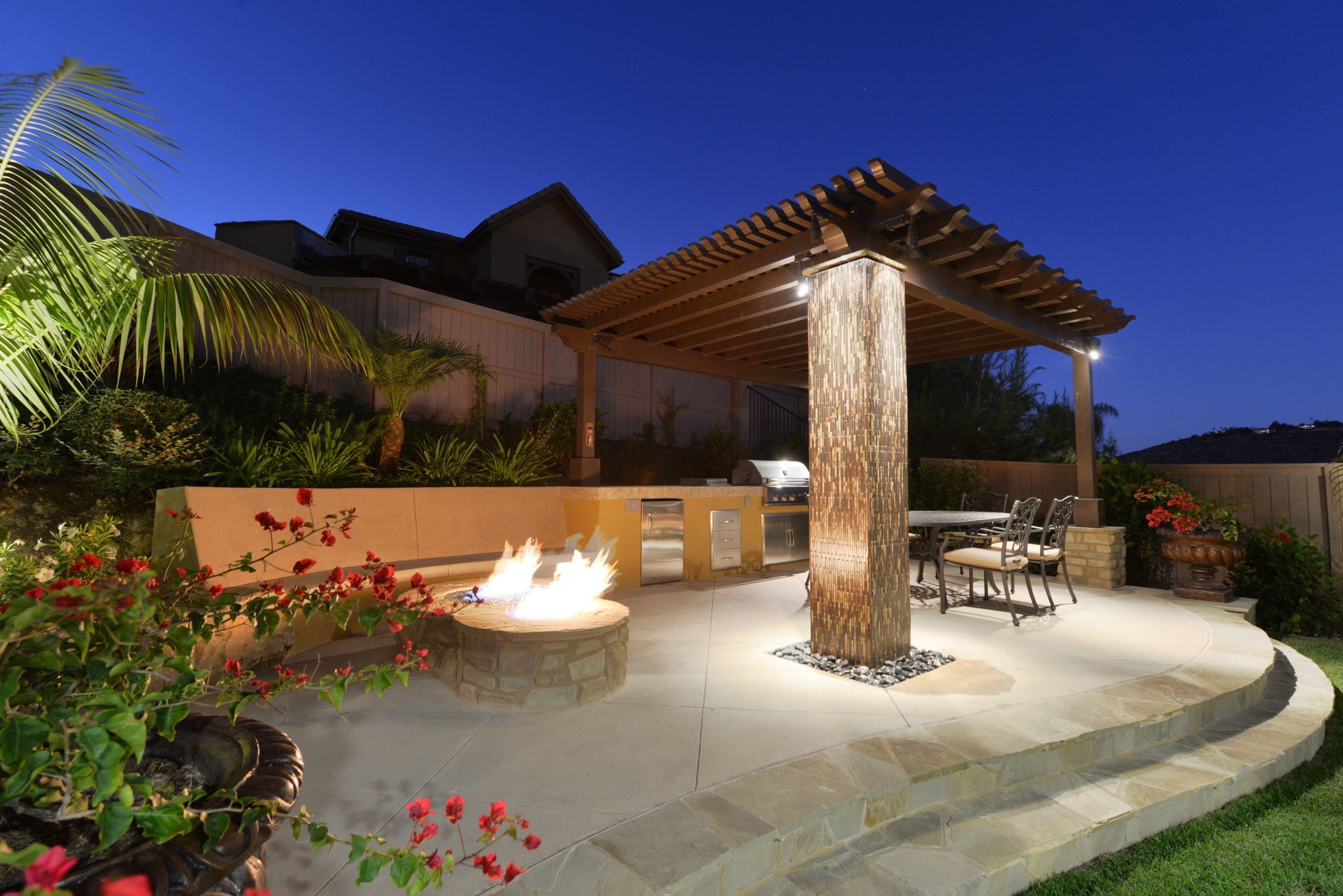 A patio with a fire pit and a pergola at night