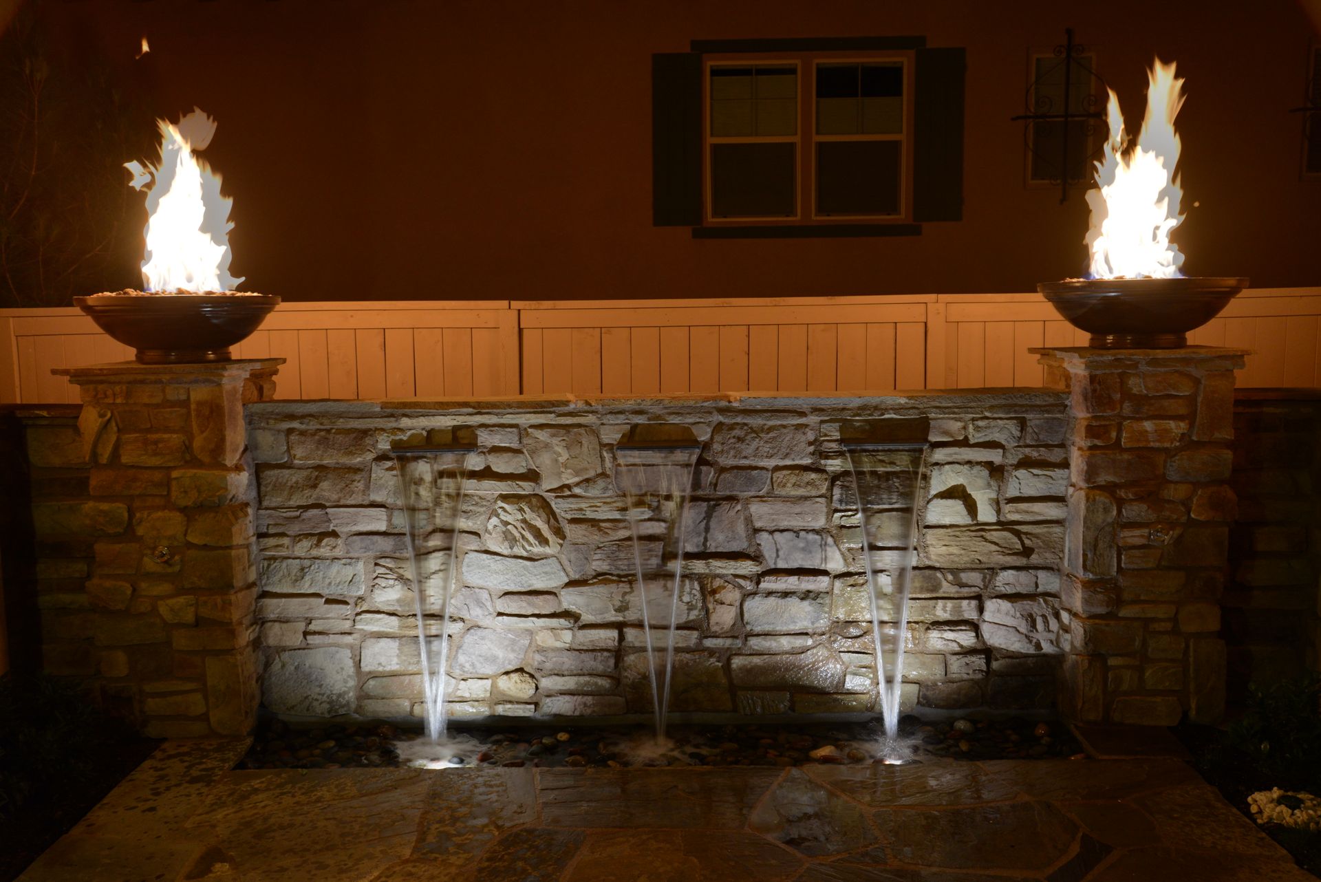 A water fountain is lit up at night in front of a house.