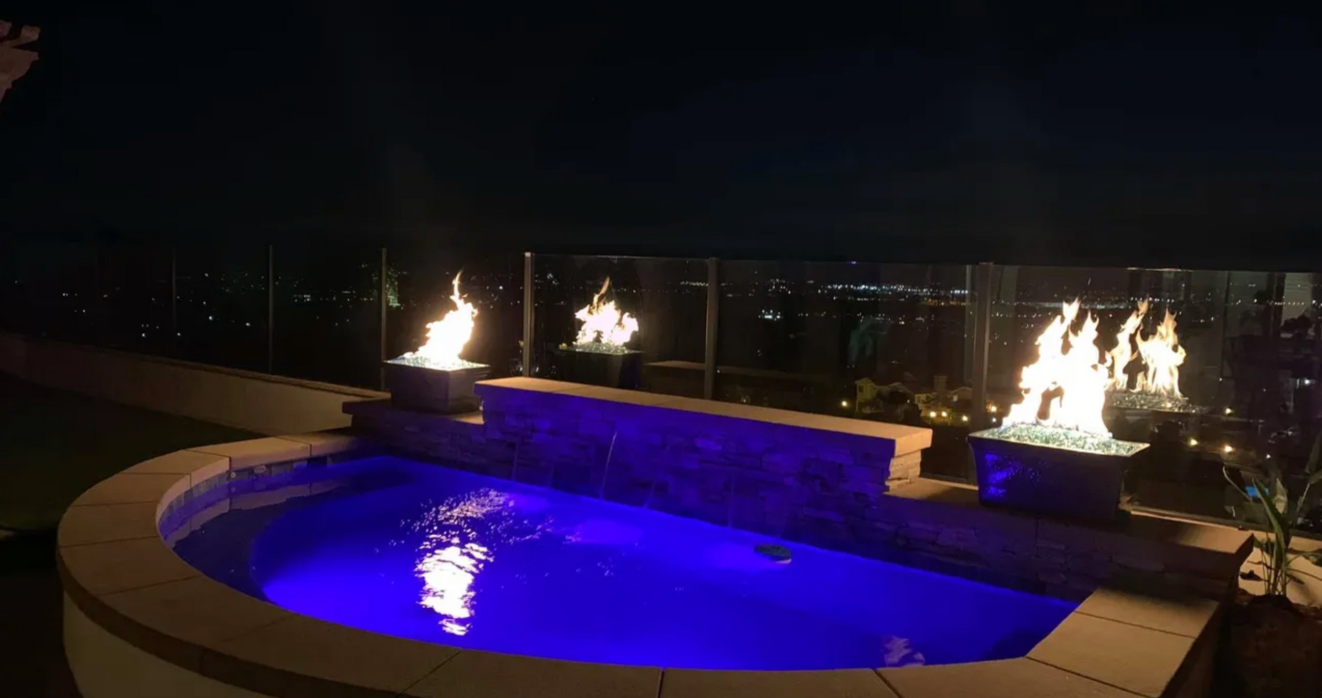 A swimming pool with a fire pit in the middle of it at night.