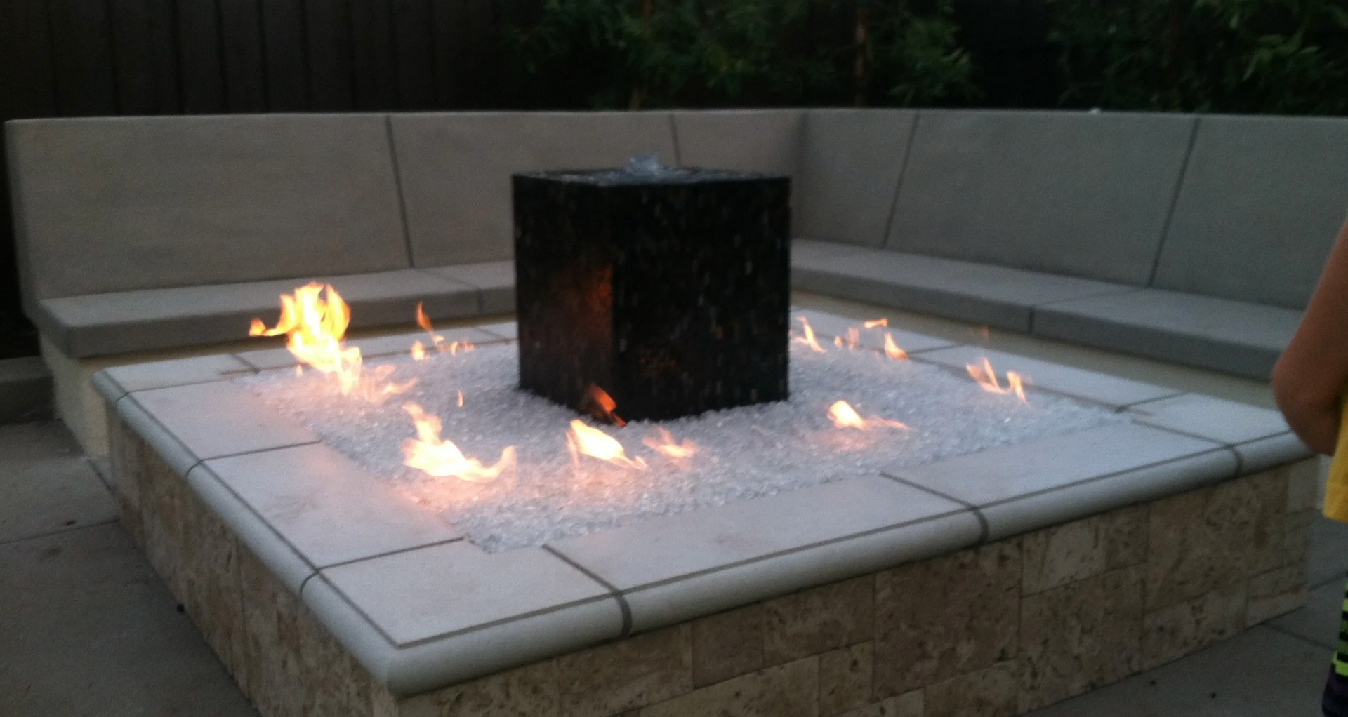 A person is standing in front of a fire pit with flames coming out of it.
