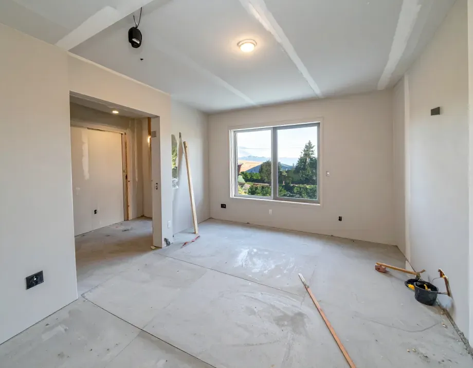 Room under renovation; gray walls and floor, window with a view, and construction materials.