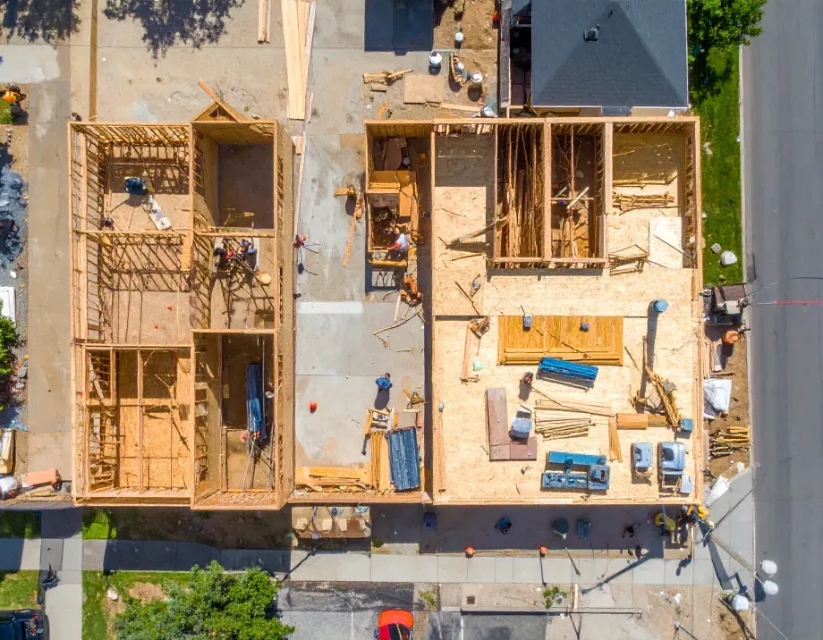 Overhead view of a new house under construction; wood framing with workers, concrete, and road.