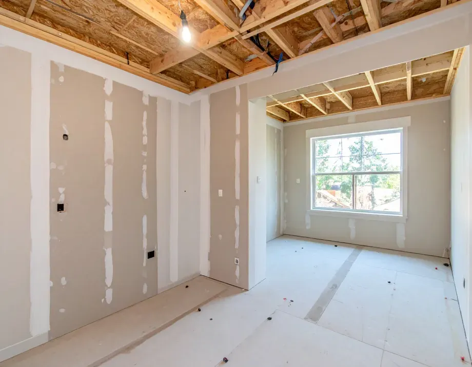 Interior of a room under construction; drywall partially installed, unfinished ceiling, window in the back.
