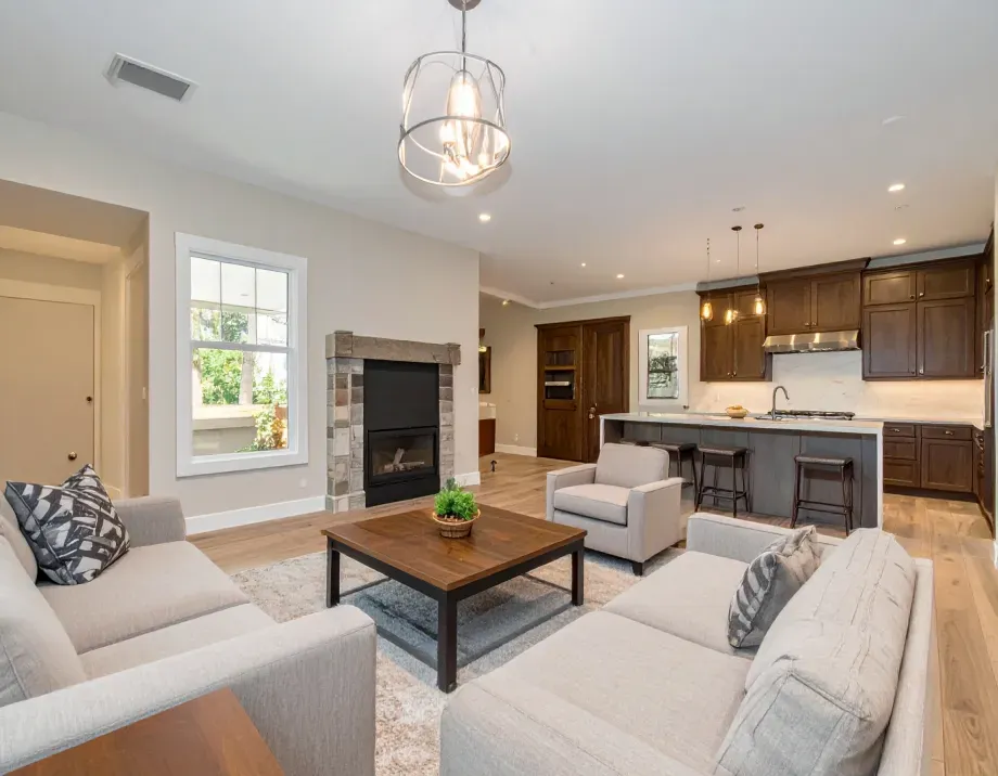 Spacious living room with fireplace, open to kitchen; neutral colors, two sofas, chairs, light fixtures.