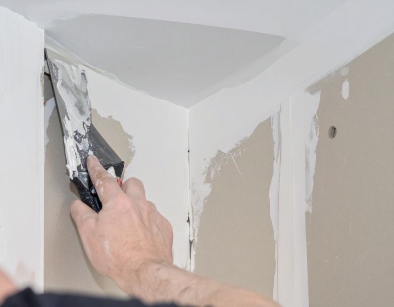 Person using a putty knife to apply drywall compound to an interior corner of a wall.