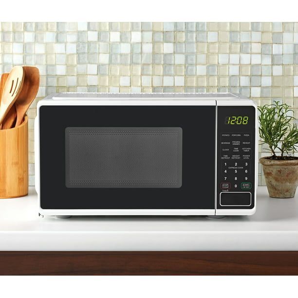 A white microwave sits on a counter with a wooden utensil holder and a small potted plant next to it.