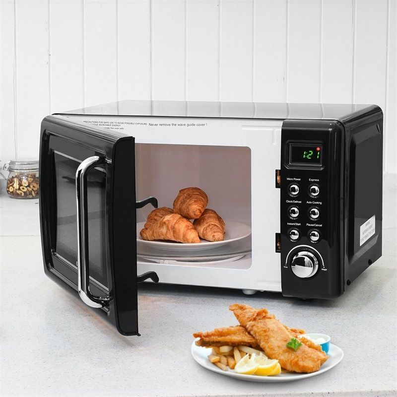 A black and white microwave on a countertop with its door open, featuring croissants inside and fried fish on a plate.