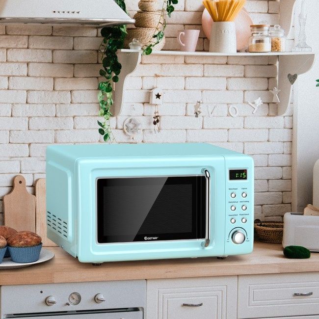 A light blue retro-style microwave sits on a wooden kitchen counter in front of a white brick wall.