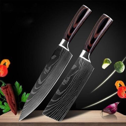 Two Damascus steel kitchen knives with dark wood handles angled on a wooden surface against a black background with produce.