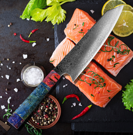 A chef's knife with a patterned blue and red handle rests on a slate board with salmon fillets, lemons, and spices.