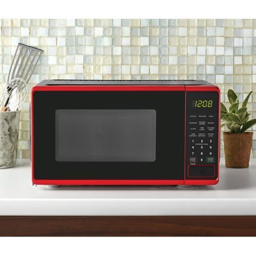 A bright red countertop microwave with a black door and digital display sits on a white counter against a tiled wall.