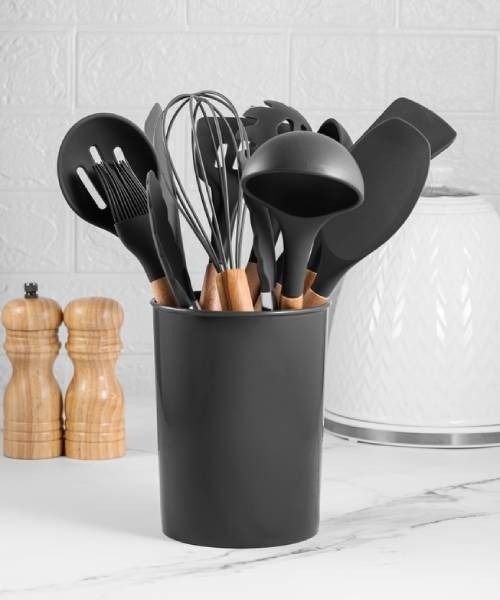 A set of black silicone kitchen utensils with wooden handles stored in a black canister on a white countertop.