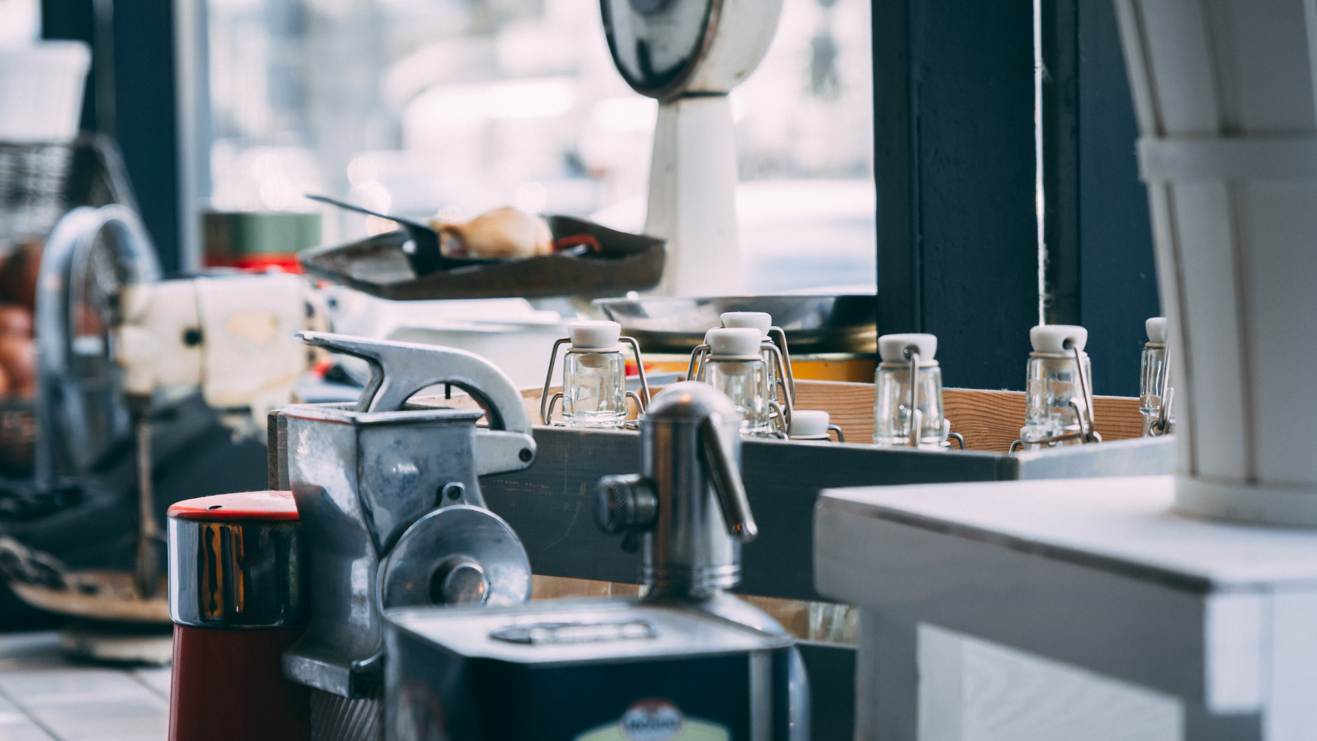 A collection of small glass jars and vintage kitchen equipment, including a metal grinder, arranged on a surface.