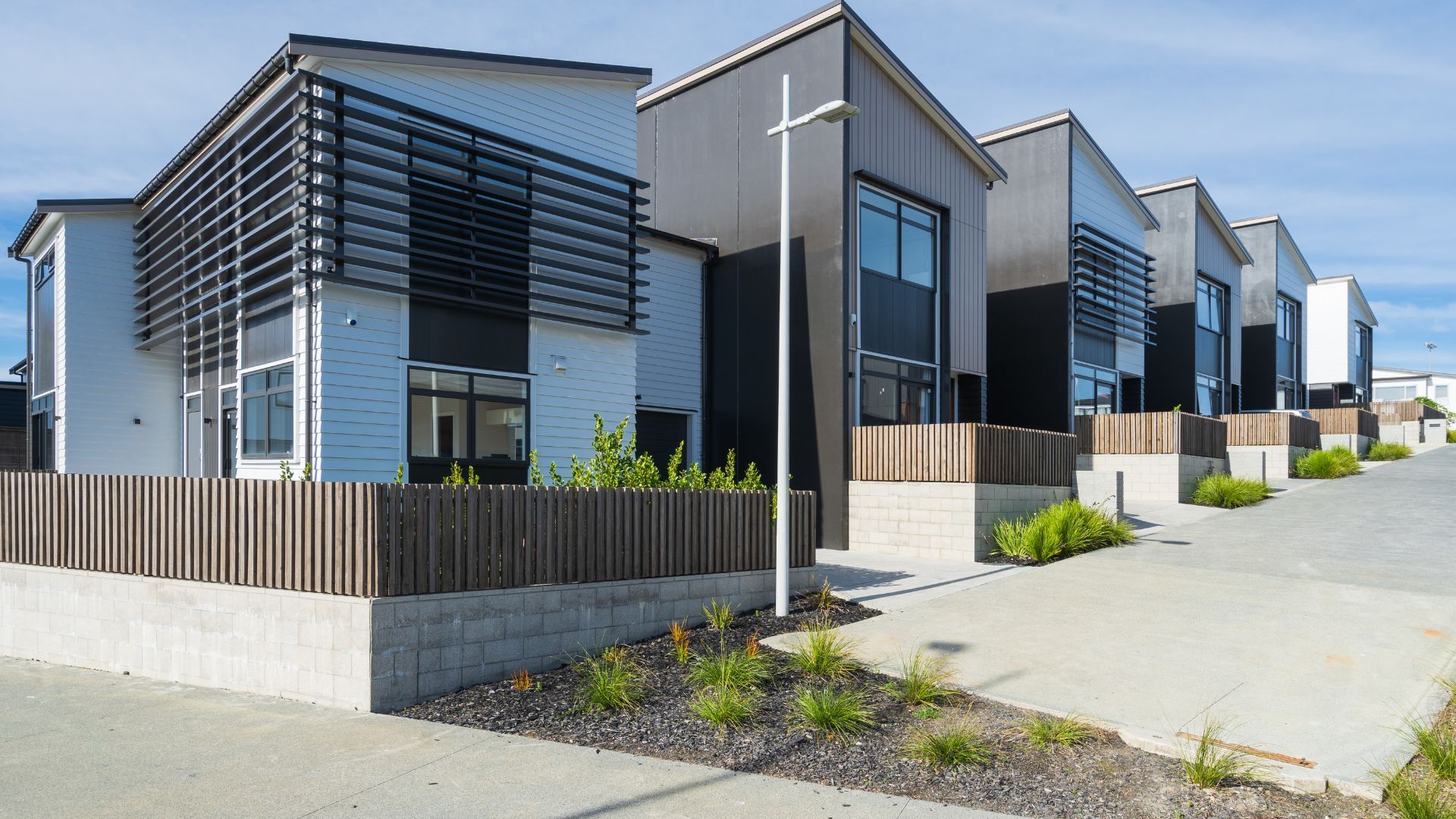 Modern row houses with gray facades, fenced patios, and a paved walkway on a sunny day