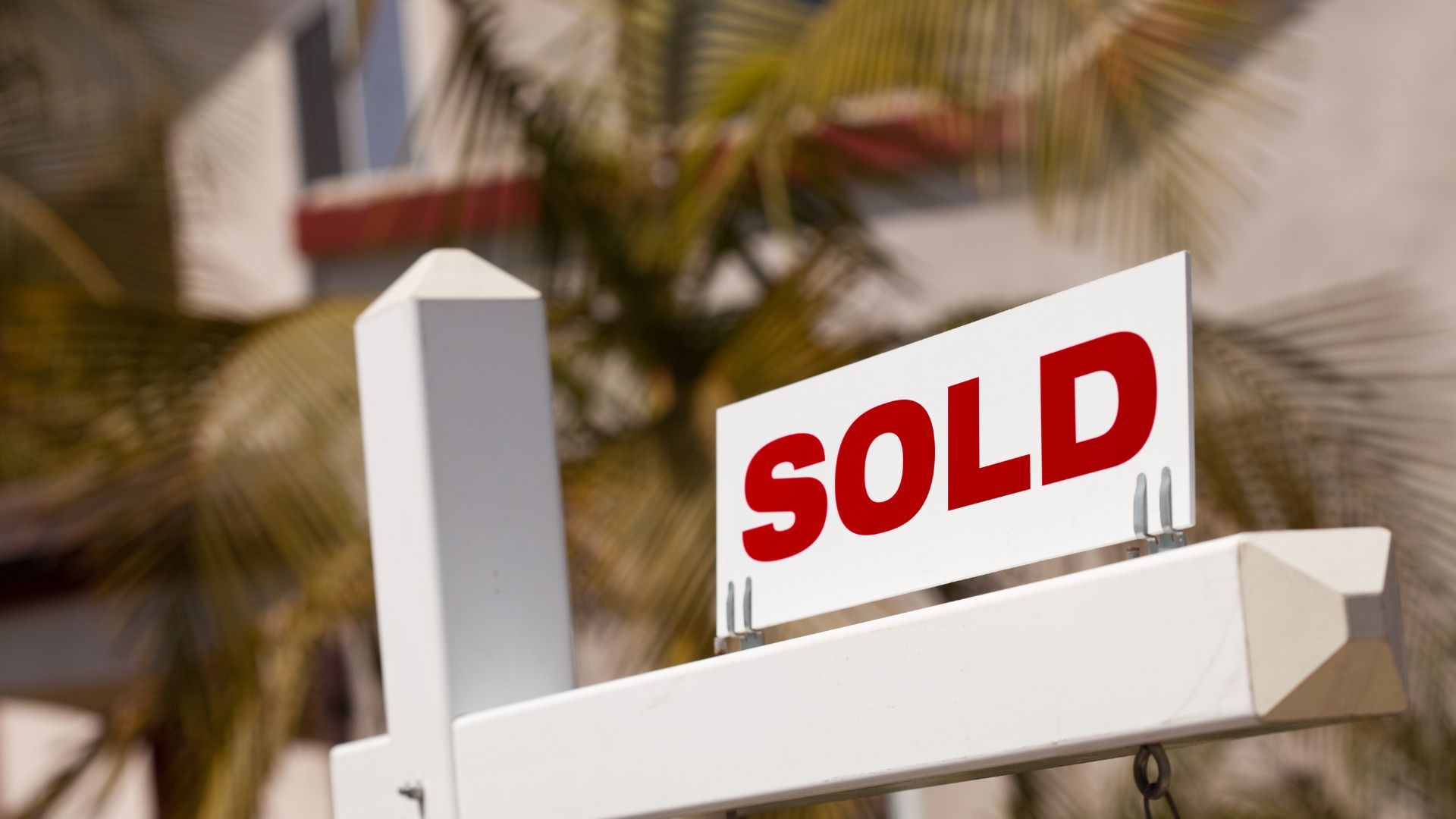 Red SOLD sign on a white real estate post outdoors