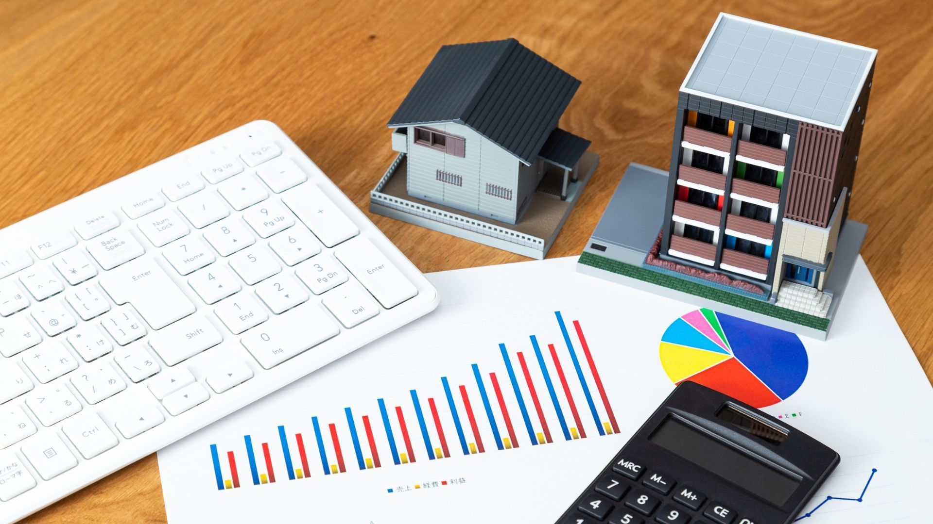 Desk with keyboard, charts, calculator, and small house models, suggesting business or real estate analysis.