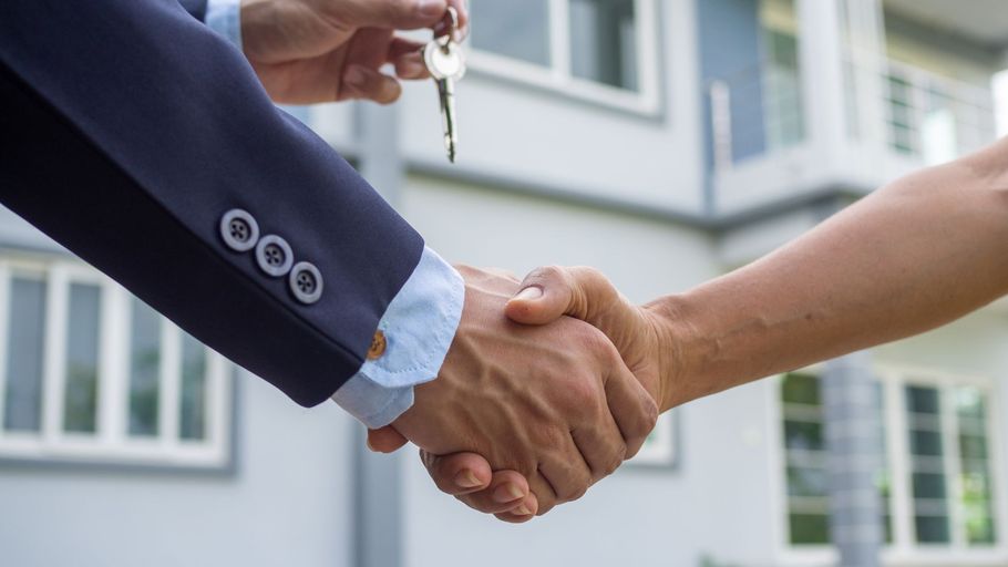 Two people shaking hands in front of a modern office building.