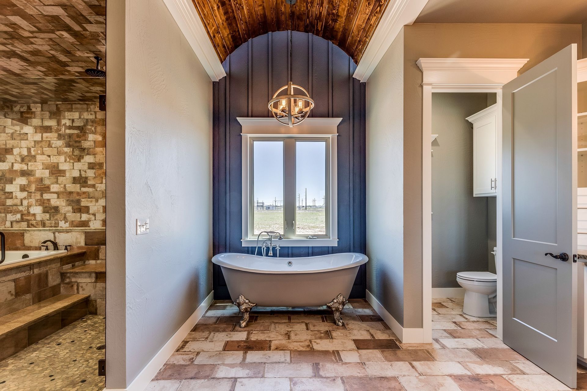 Bathroom with a clawfoot tub under a window, tiled floor, and a separate toilet alcove
