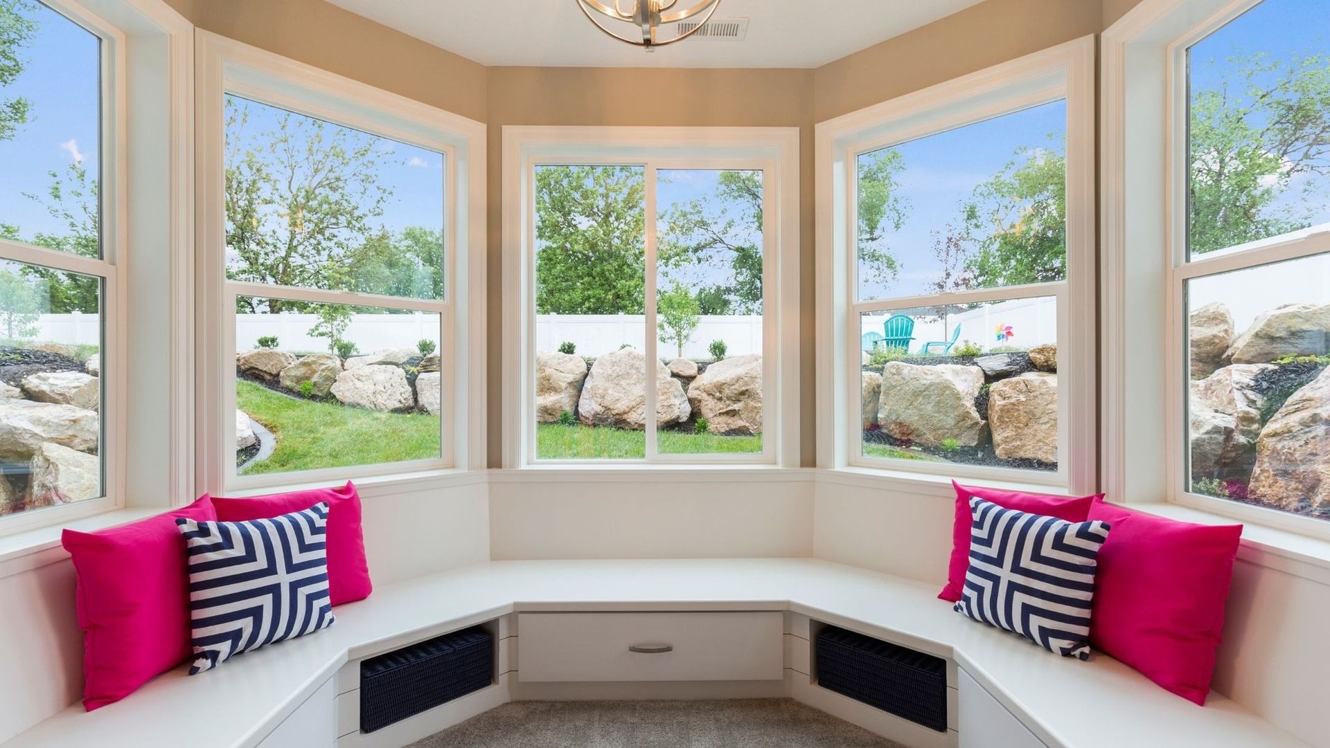 Bright bay window seating nook with pink pillows overlooking a green landscape