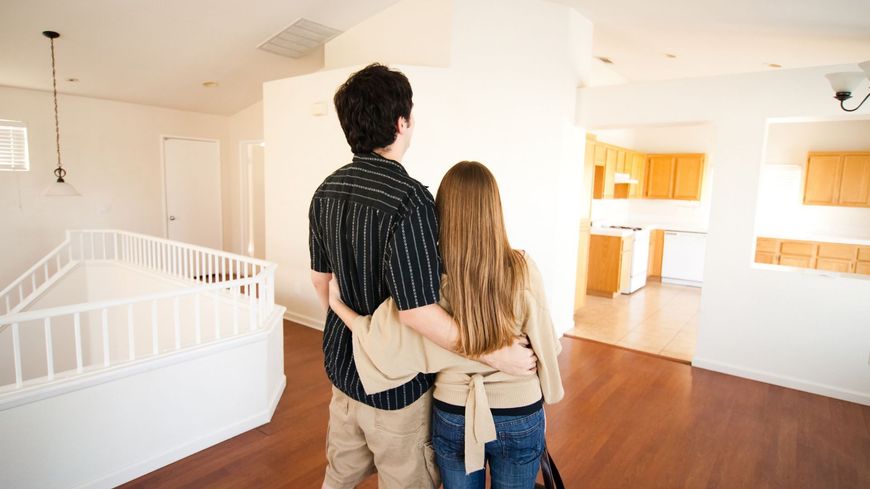 Couple standing arm-in-arm in a bright, empty house with white walls and wood floors