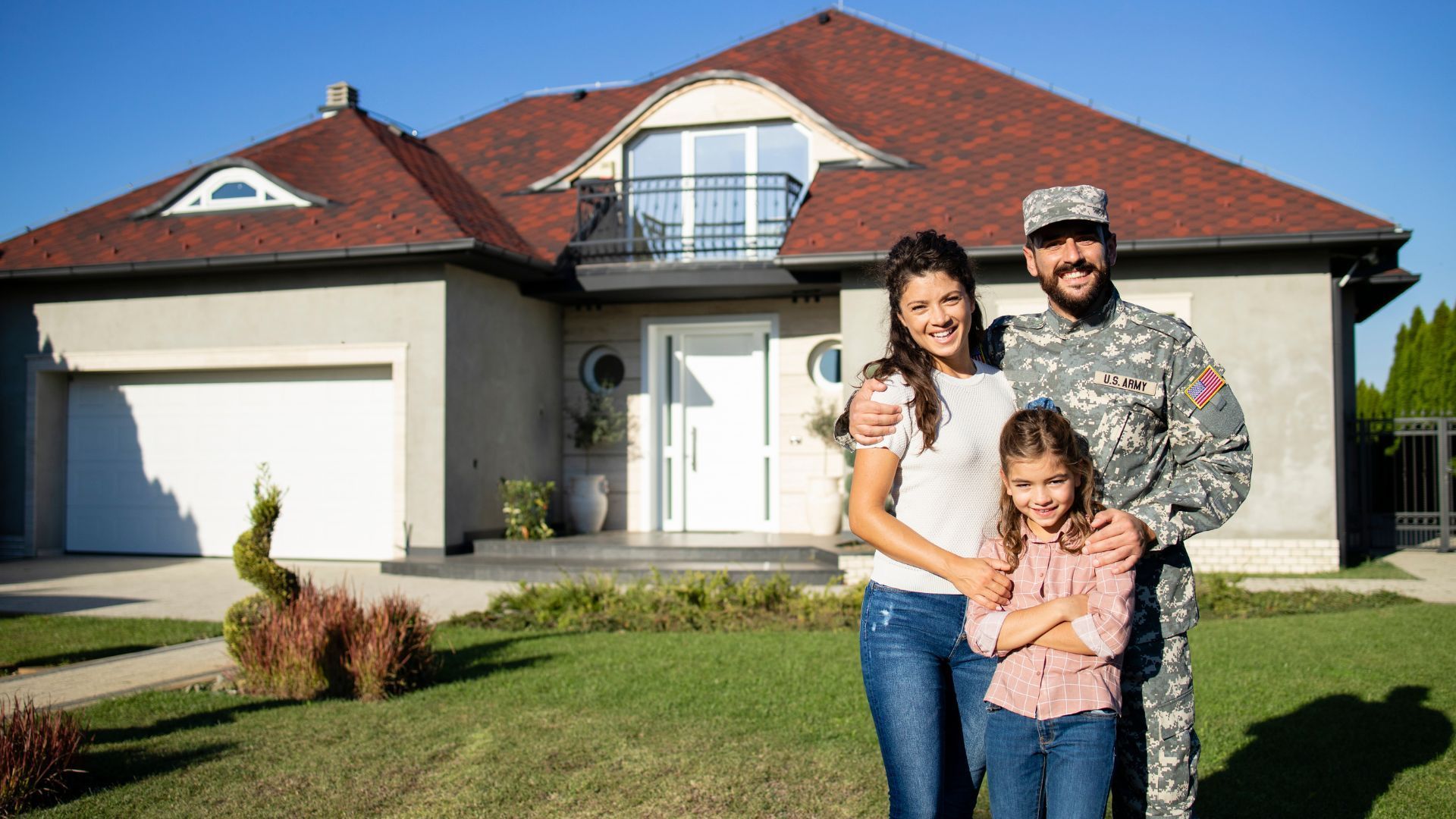 Family standing in front of a house with a red roof and garage on a sunny day.