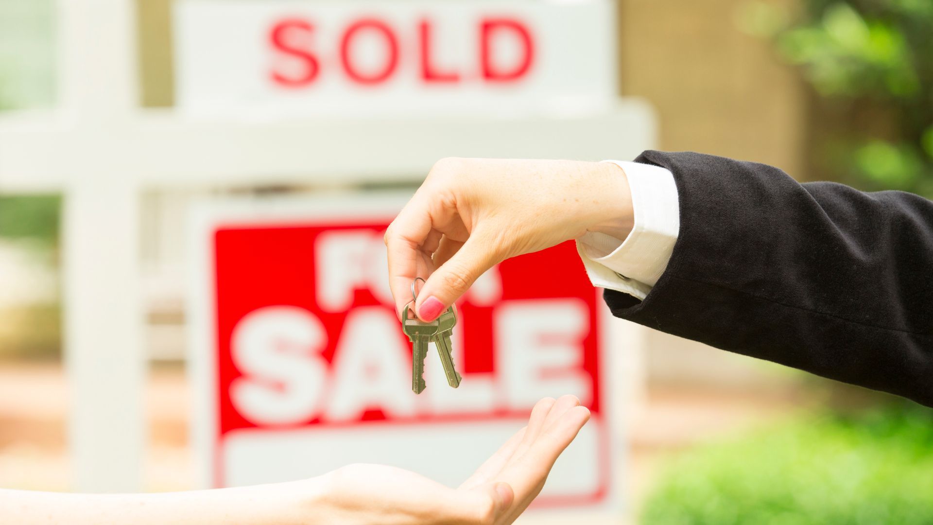 Hand placing SOLD sign in front of red SALE sign on a house window