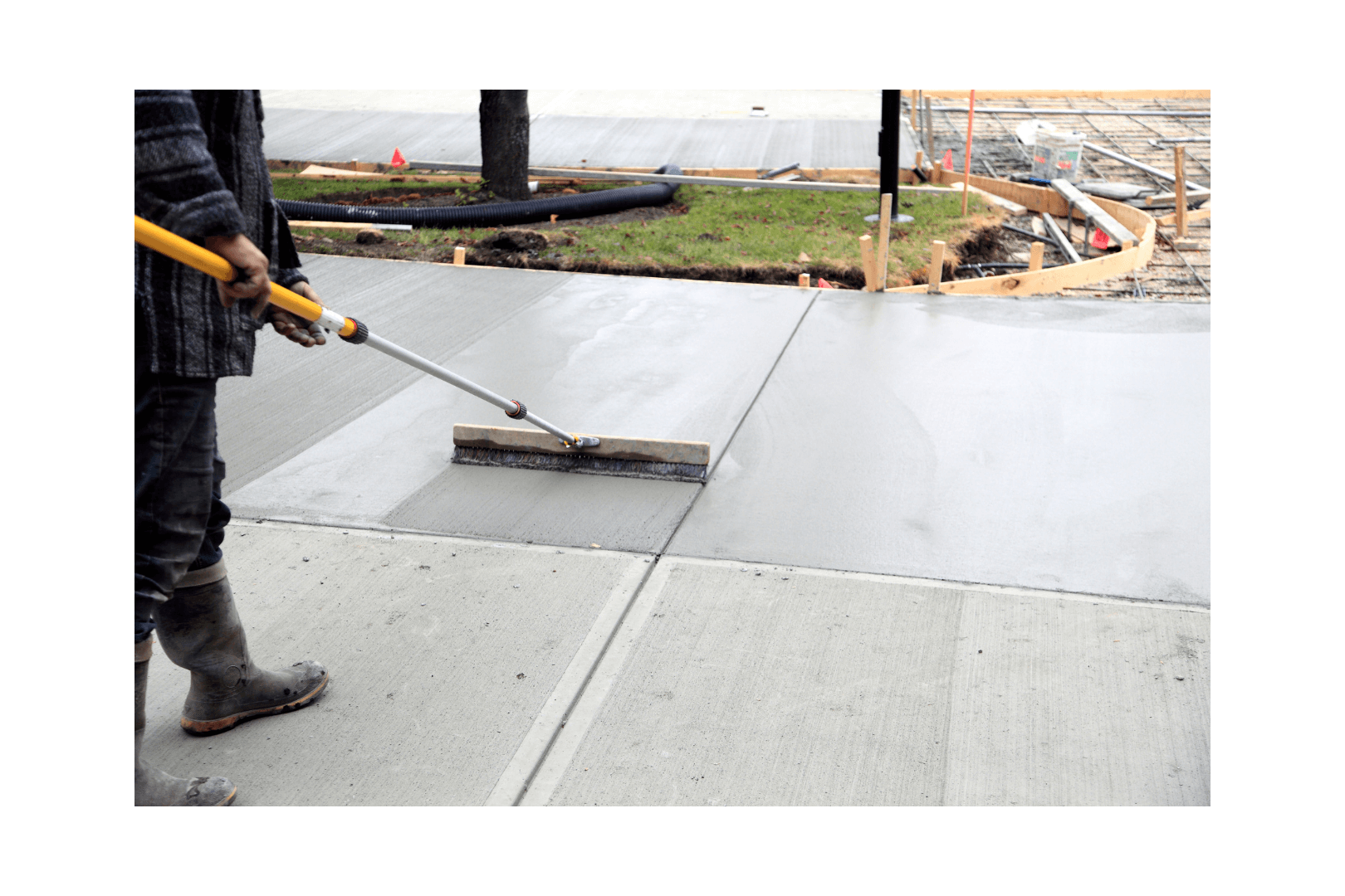 Freshly poured concrete sidewalk, framed by wooden forms, in a construction setting with surrounding dirt.